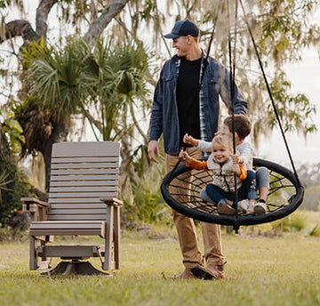 man pushing kids in a swing next to glider chair