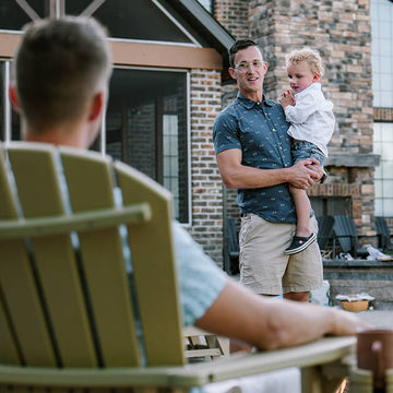 man holding child talking to another man in a chair