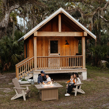 family sitting in Adirondack chairs around a fire table front of a small cabin 